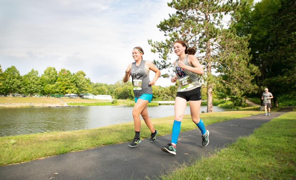 Two girls running in a race, on a path with a creek beside the path on a nice day in the summer