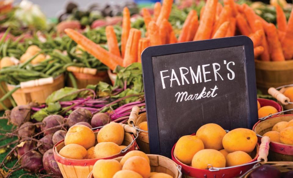 A photo of several baskets filled with various fruits and veggies with a chalk board sign which reads Farmer's Market