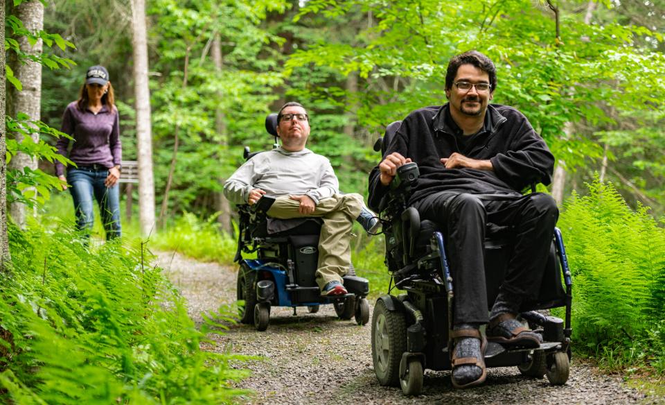 Three people heading down a trail in the woods, two of them are in wheelchairs