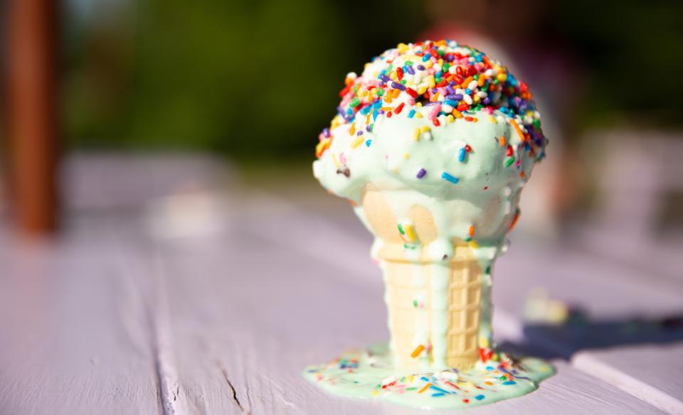 An ice cream cone on a table with the ice cream melting down the side