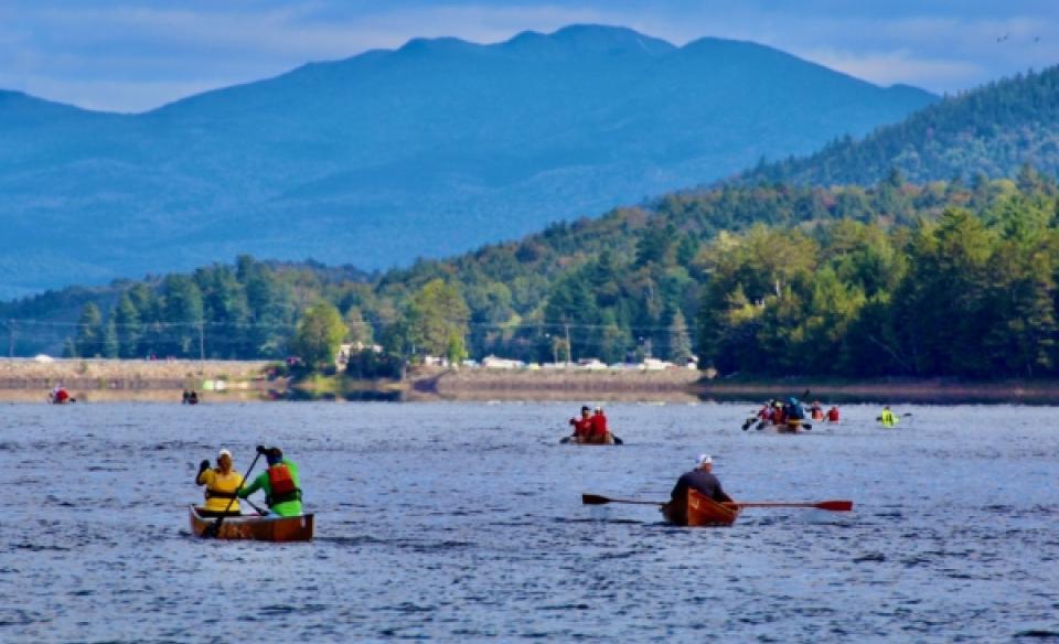 Long boat paddlers on the water with the mountains in the background