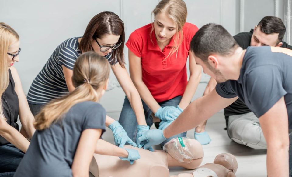 A CPR instructor teaching skills to a class as they sit around a CPR dummy