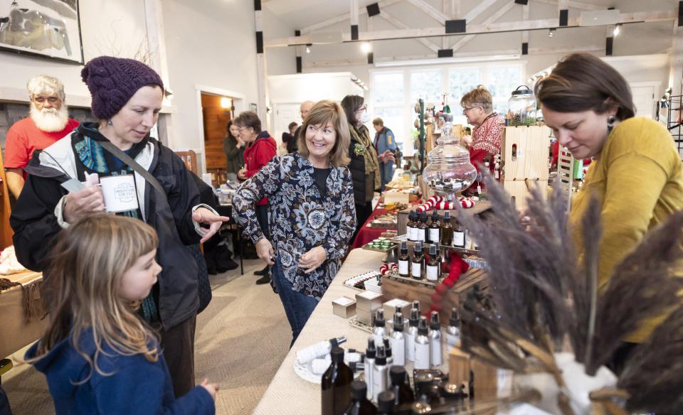 People at an indoor craft fair shopping with artisand behind their display table