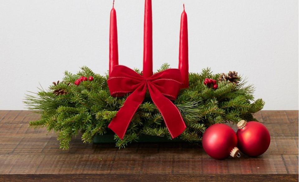 a table centerpiece made from balsam fir branches decorated with a reed bow and three red candles