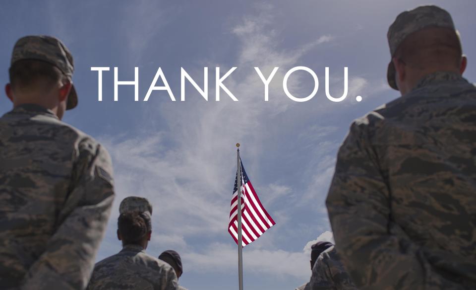 A photo of several military members standing facing an American flag in front of them with the words 