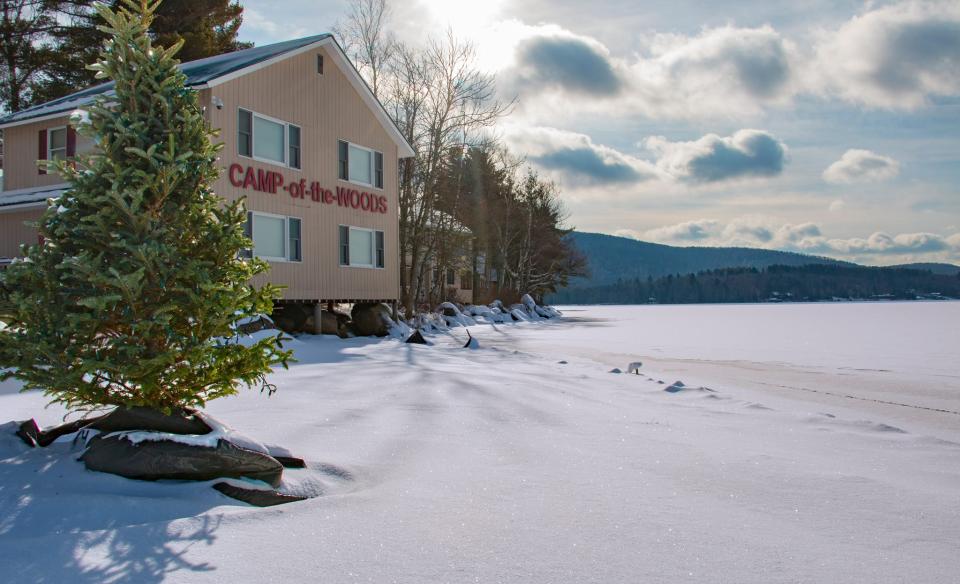 A phot of a builing with Camp of the Woods on the front, on a winter day with sunshine and fresh snow.