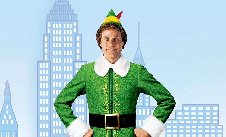 A photo of Buddy the elf standing in front of a drawing of the NYC skyline