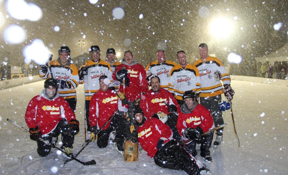 Two teams of hockey players posing for a photo on the ice with snow falling