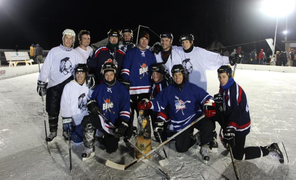 Two teams of hockey players posing for a photo on the ice