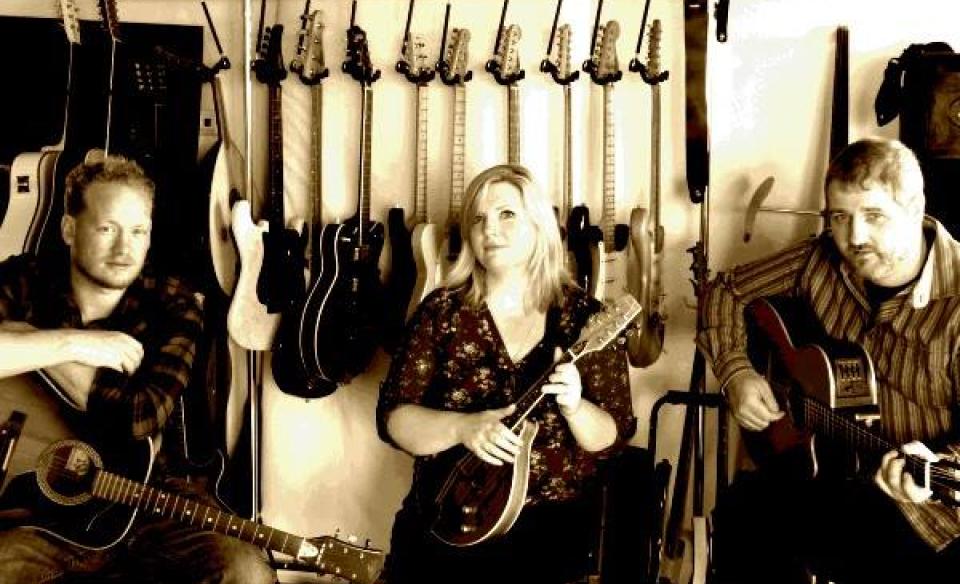 the group wayward folk, two men with guitards and a woman with a smaller stringed instrument sitting and posing for the photo