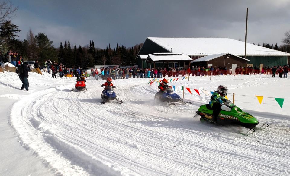 several kids racing mini snowmobiles taking a turn on the snow track