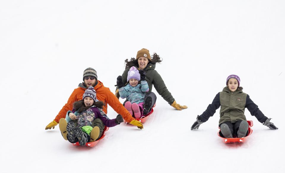 a family sledding down the hill on different sleds