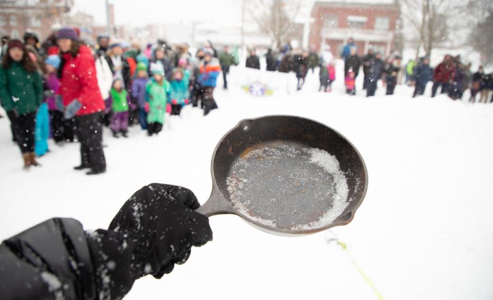 a woman holding a frying pan with a crowd watching in the back ground