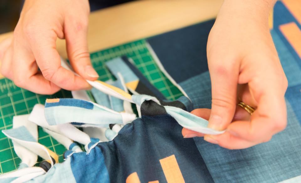 a person tying the ends to make a no-sew blanket