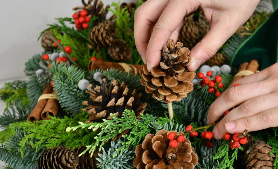 a person adding pines cones to a hand made pine wreath