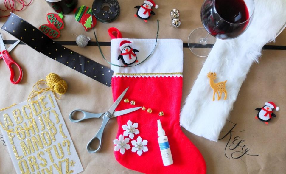 A red Christmas stocking with craft items, scissors, and glue all around in preparation to decorate the stocking