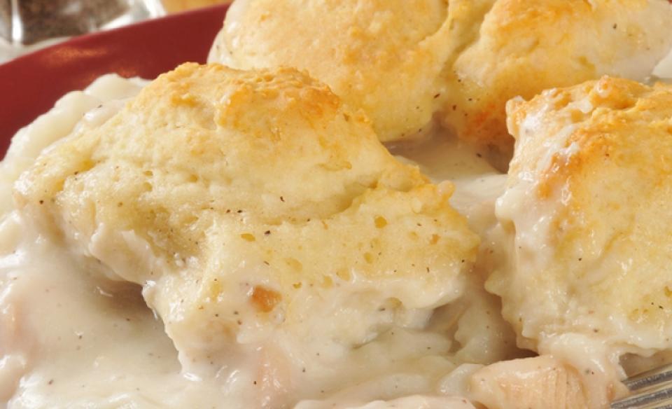 A red plate with chicken in gravy with a few biscuits on the side