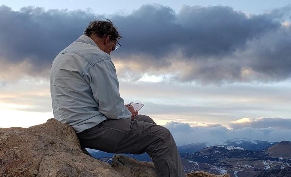 Phil Bayly sitting on top of a mountian writing in a note pad.