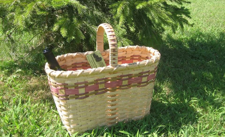 a hand-made wine basket with 2 bottles of wine in it sitting on green grass