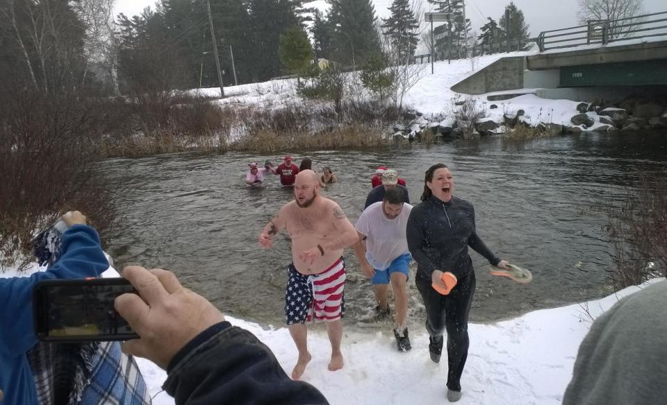 Several people coming back on to a snowy shore after going into the cold winter waters for a polar plunge