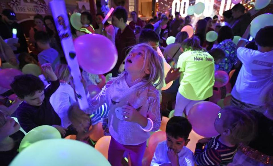 kids playing in a room with black lights glowing and balloons falling