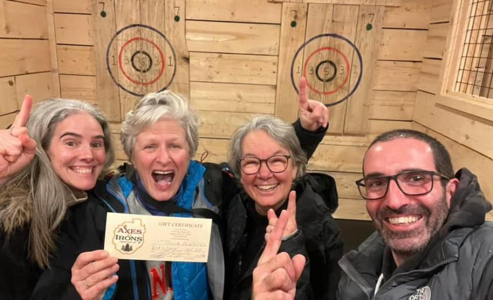 four people posing infront of the axe throwing bullseye holding a gift certificate and very excited about winning it