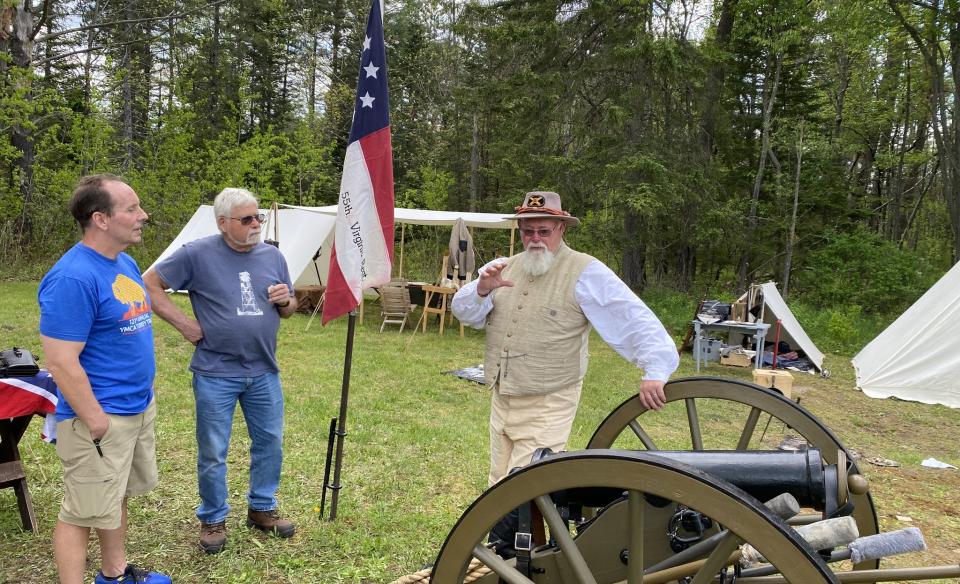 A man in period dress talking with two other men about a civil war canon