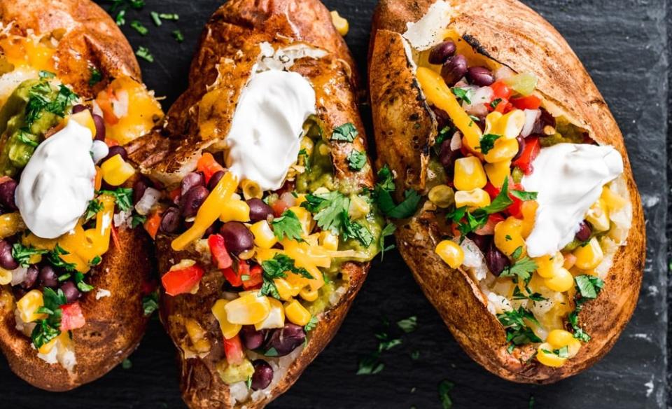 A photo of three baked potatoes loaded with a variety of toppings