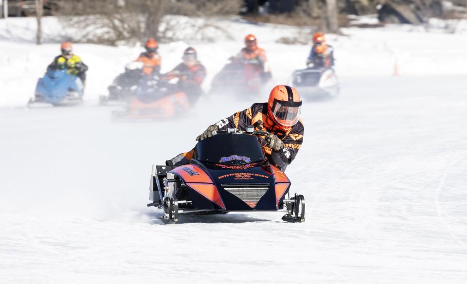 a snowmobiler leads a group of others in a race going into a turn