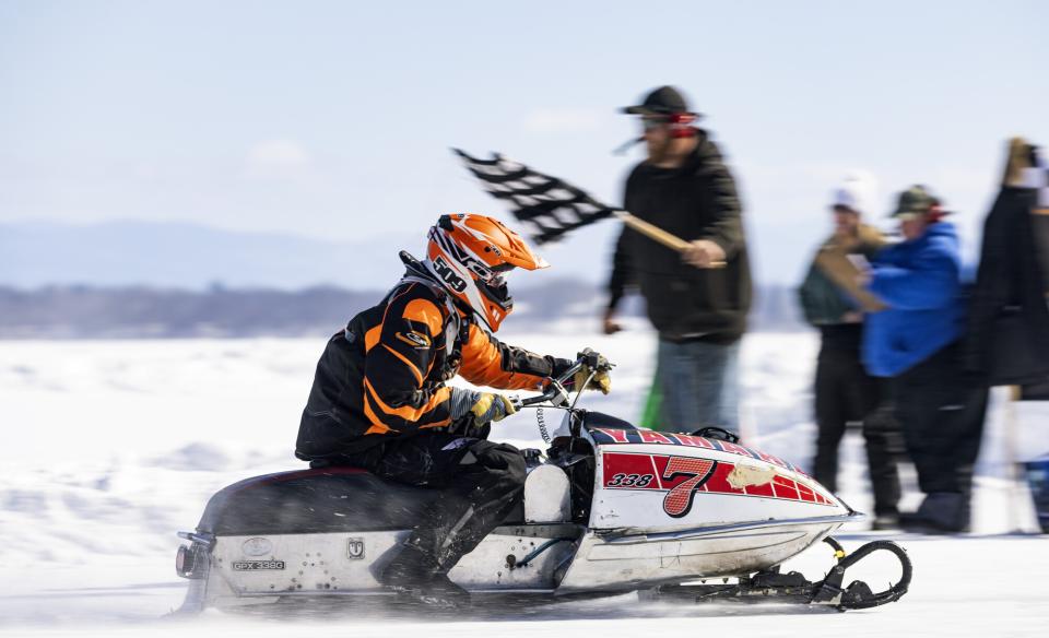 A snowmobiler riding past a man waving a checkered flag at the end of the race