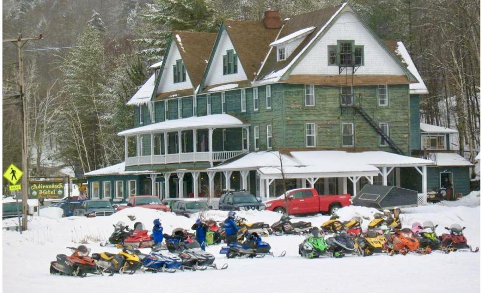 An exterior photo of the Adirondack Hotel in Winter with many snowmobiles parked outside