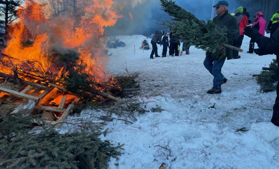 A man throwing another Christmas tree on the bonfire