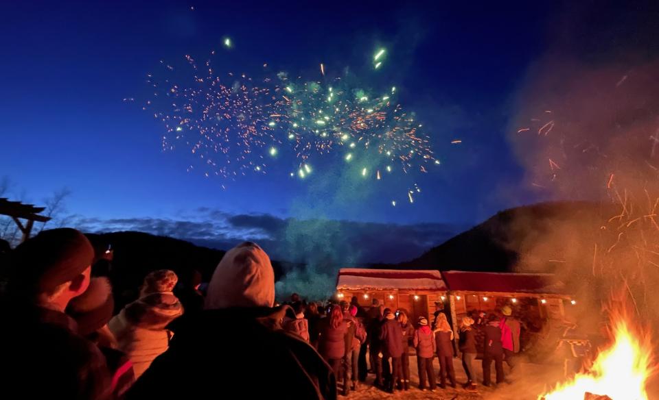 Fireworks bursting in the night sky as people watch standing around the bonfire