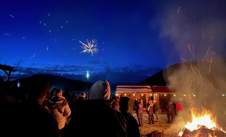 Fireworks bursting in the night sky as people watch standing around the bonfire