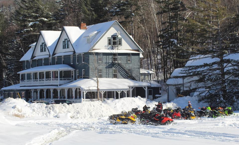 Outside photo of the ADK Hotel in winter with several snowmobiles parked outside