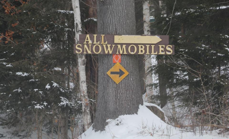 A sign on a tree that reads- All Snowmobiles with an arrow pointing right