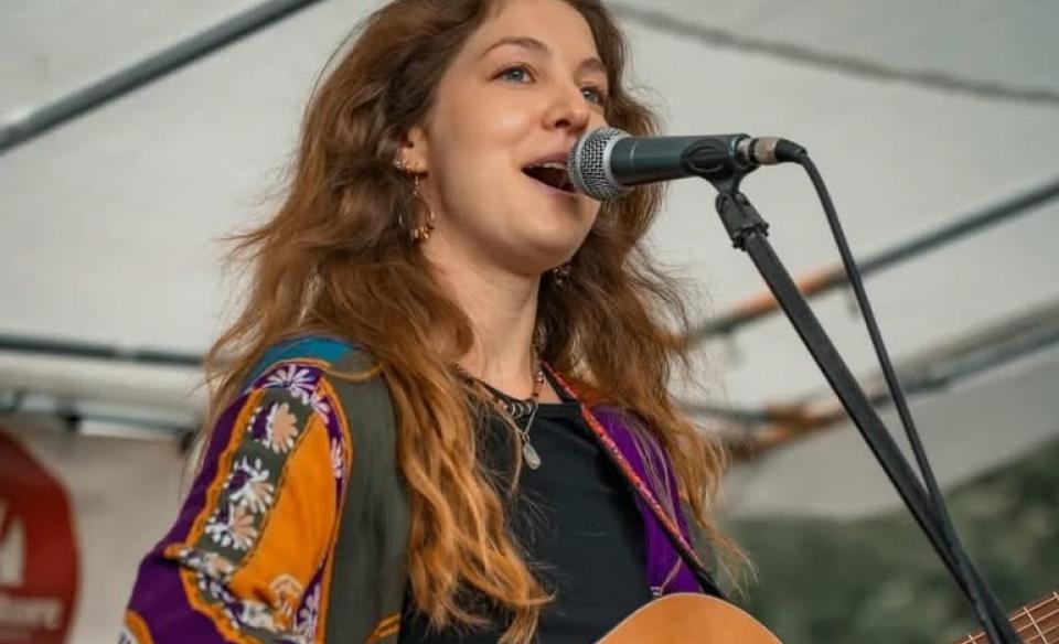 A photo of Jessie singing into a microphone and playing her guitar