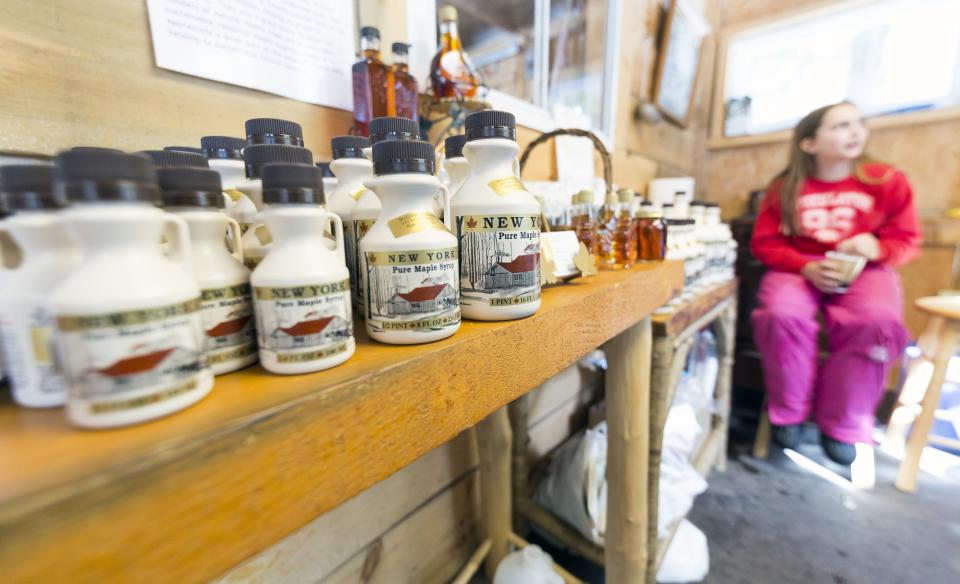 Girl sitting at the end of a table with many maple syrup bottles for sale