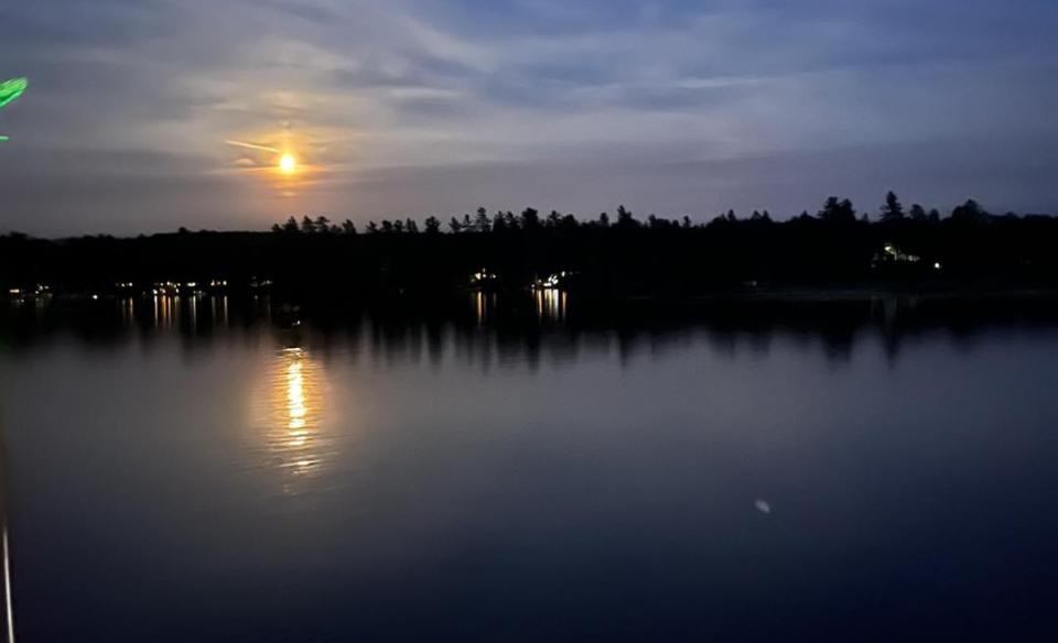 The moon shining brightly in the sky reflecting into Raquette Lake