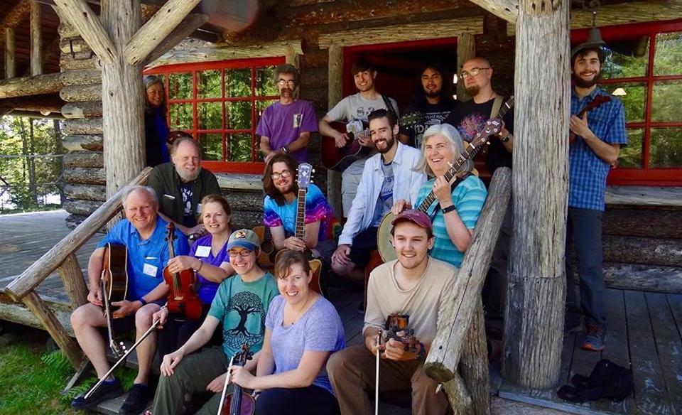 Group of people sitting and standing on the porch at Great Camp Sagamore holdong their instruments