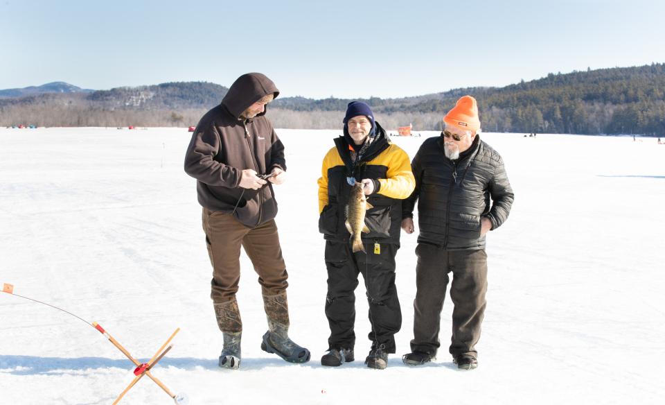 Three men holding a fish on a frozen lake.