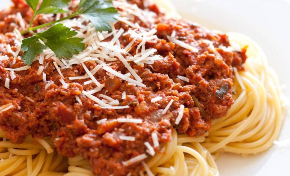 A white plate with spaghetti topped with a red meat sauce and sprinkled with parm cheese.