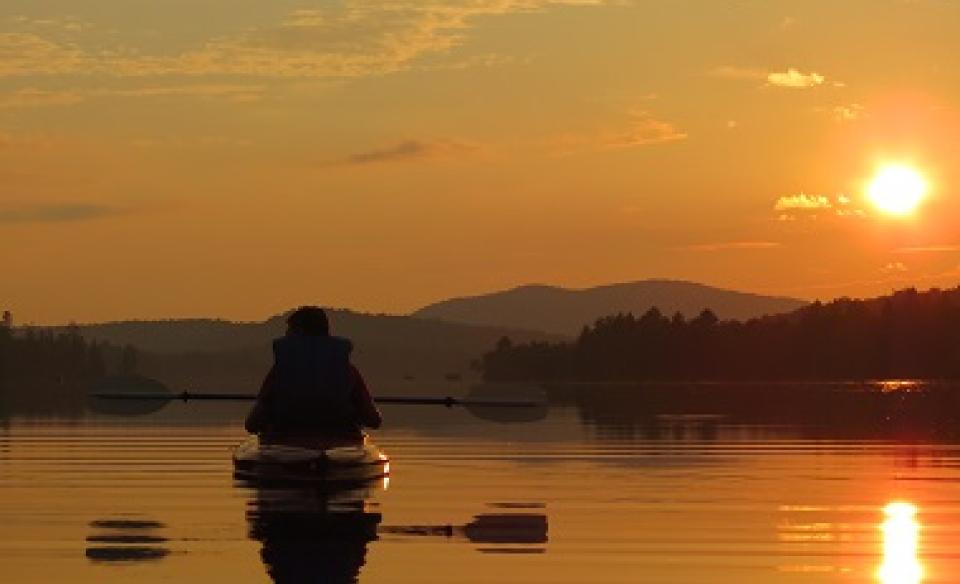 A person paddling on Lake Durant while the sunset paints the mountain sky orange.