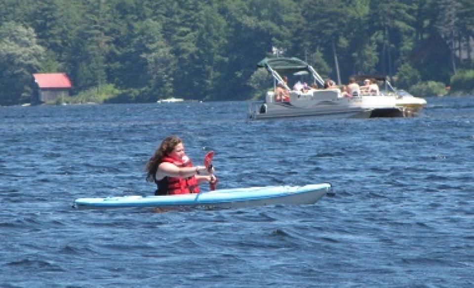 A woman in a blue kayak paddles on Piseco Lake