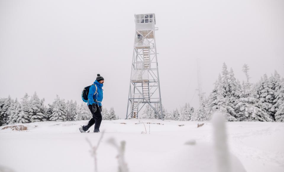 A man walks in front of a firetower in the winter