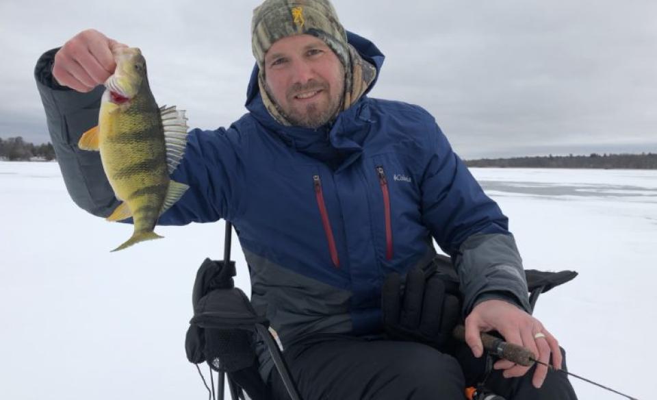 Man holding a perch on the ice.