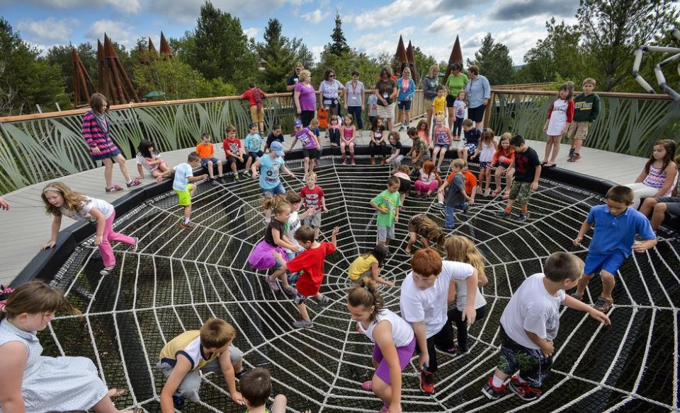 Dozens of children playing on the outdoor spiderweb exhibit