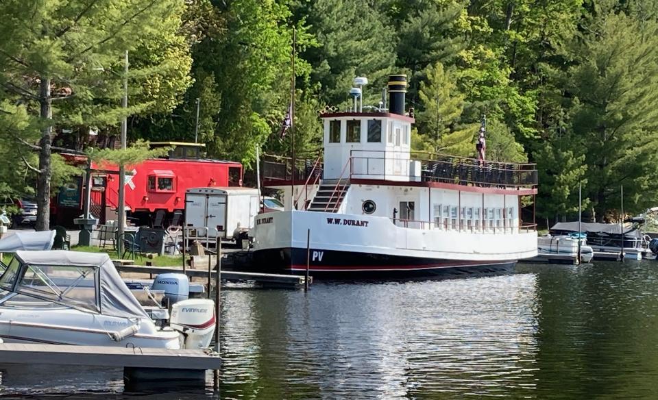 An old white and red steam boat on the water next to a red train car.