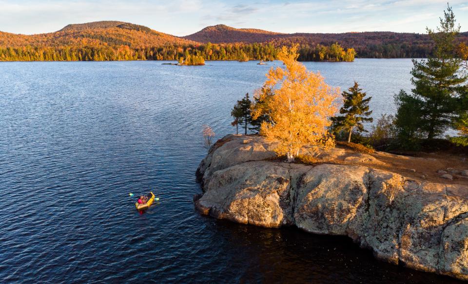 An aerial photo of a pack rafter in a lake next to an island during sunset.