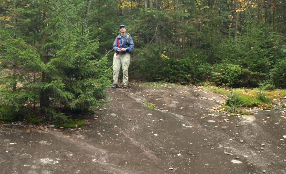 A man standing at the top of a sloped rock feature in the Moose River Plains.